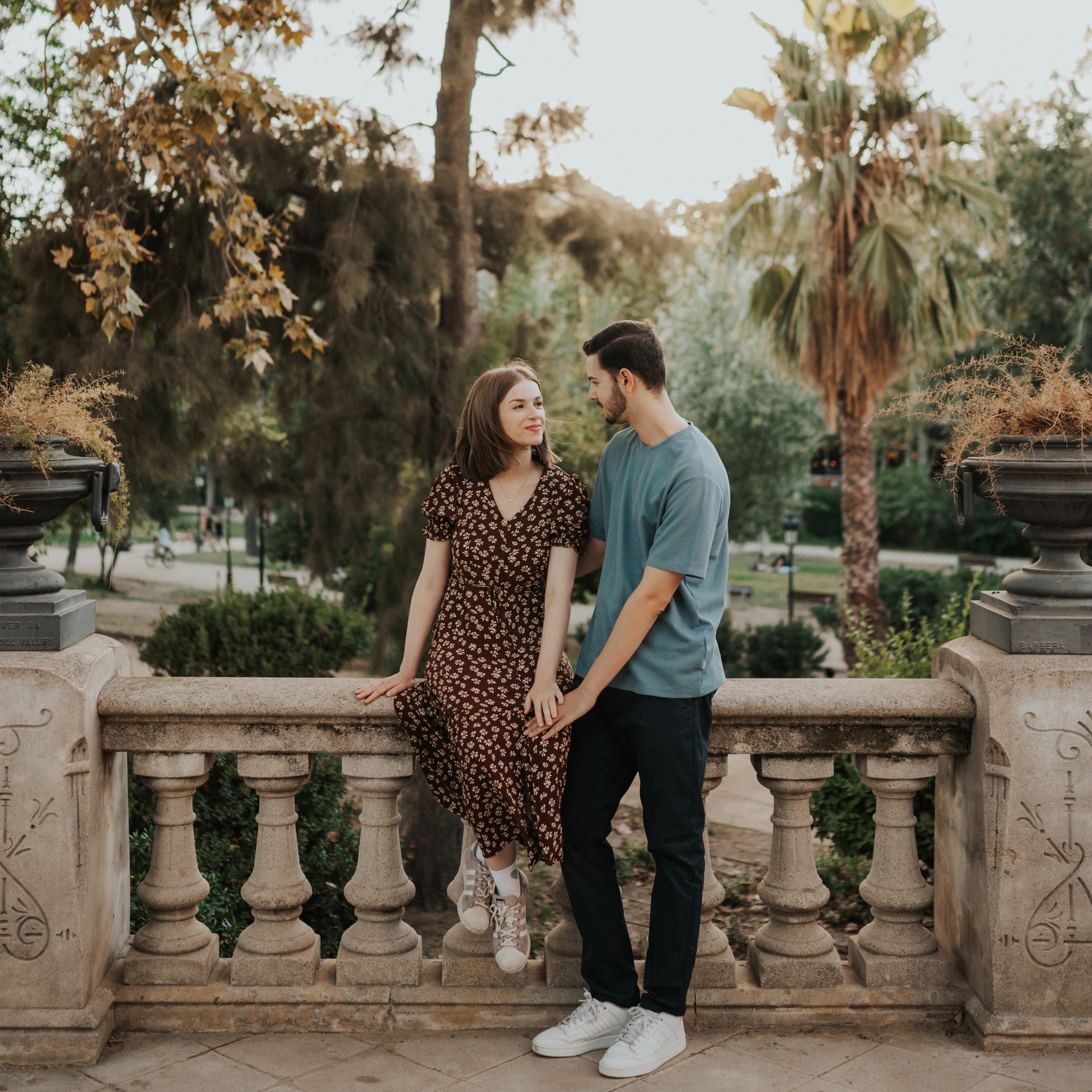 Una pareja posa junta junto a una balaustrada de piedra entre palmeras en el Parc de la Ciutadella durante una sesión de fotos de pareja en Barcelona.