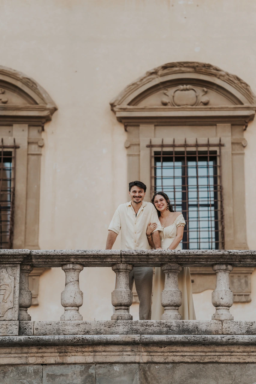 Couple leaning on a stone balustrade in front of an ornate window during their Arezzo photoshoot.