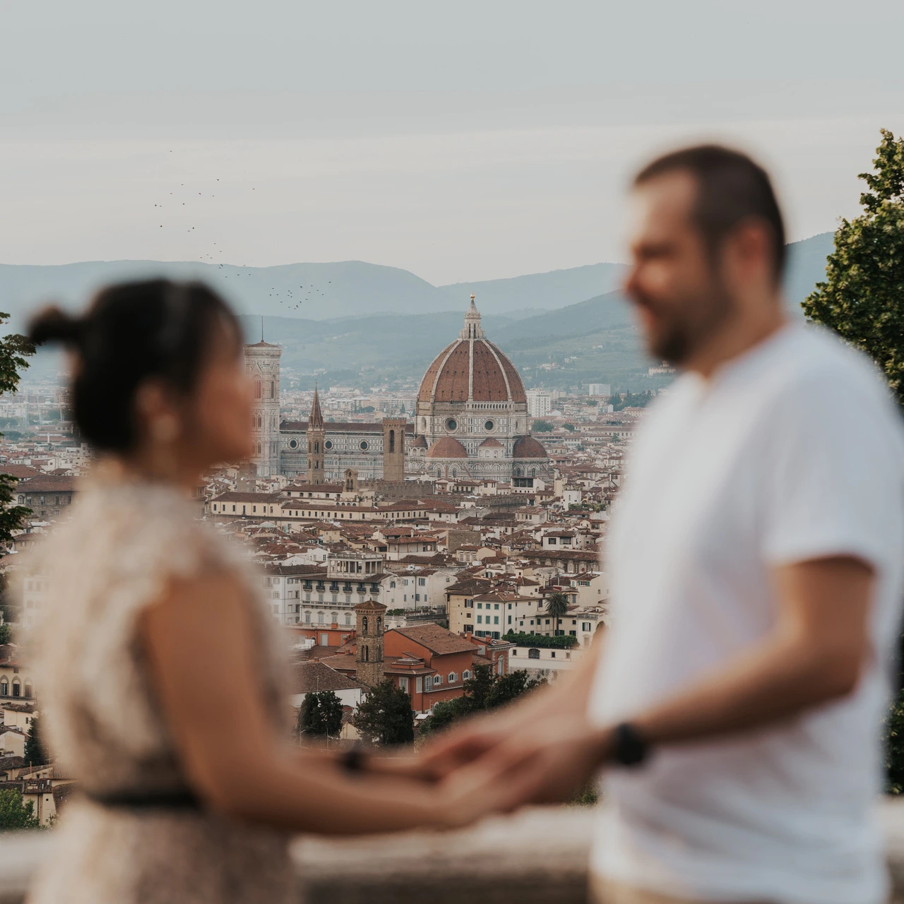 Duomo we Florencji jest ostre, a trzymająca się za ręce para na pierwszym planie celowo nieostra podczas sesji zdjęciowej przy San Miniato al Monte.