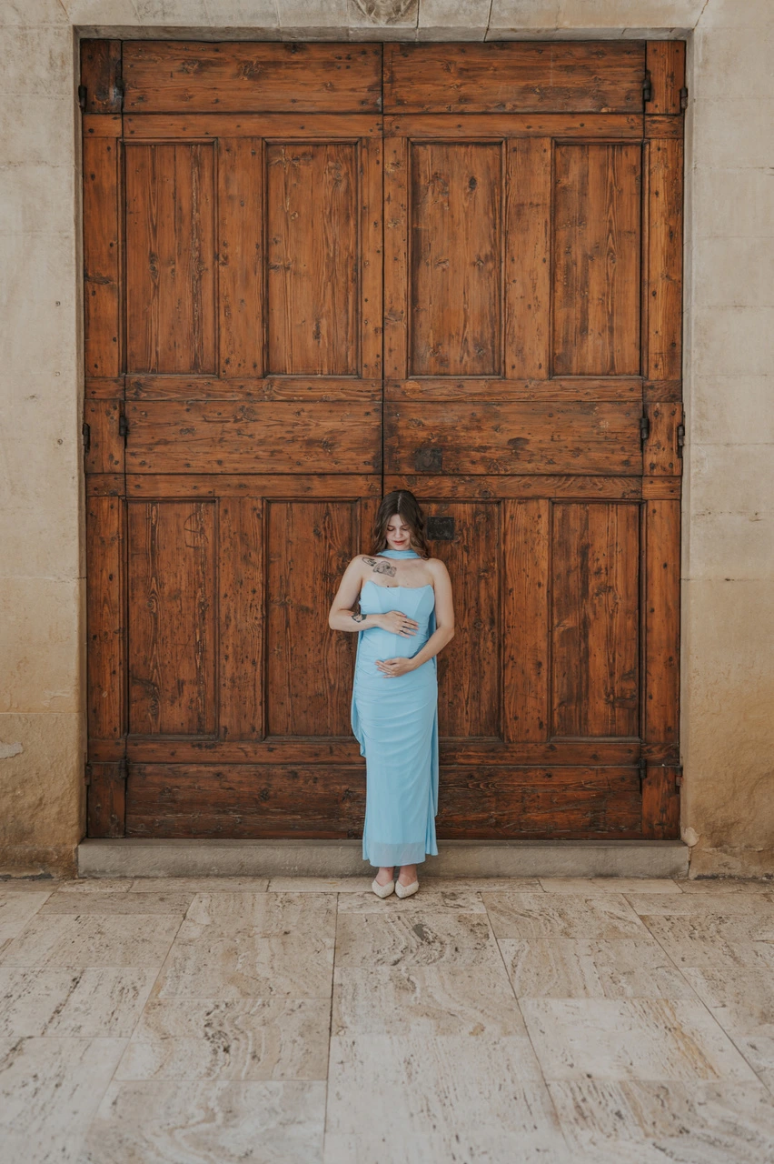 Mère en robe bleue tenant son bébé devant une grande porte en bois lors d’une séance photo à Arezzo.