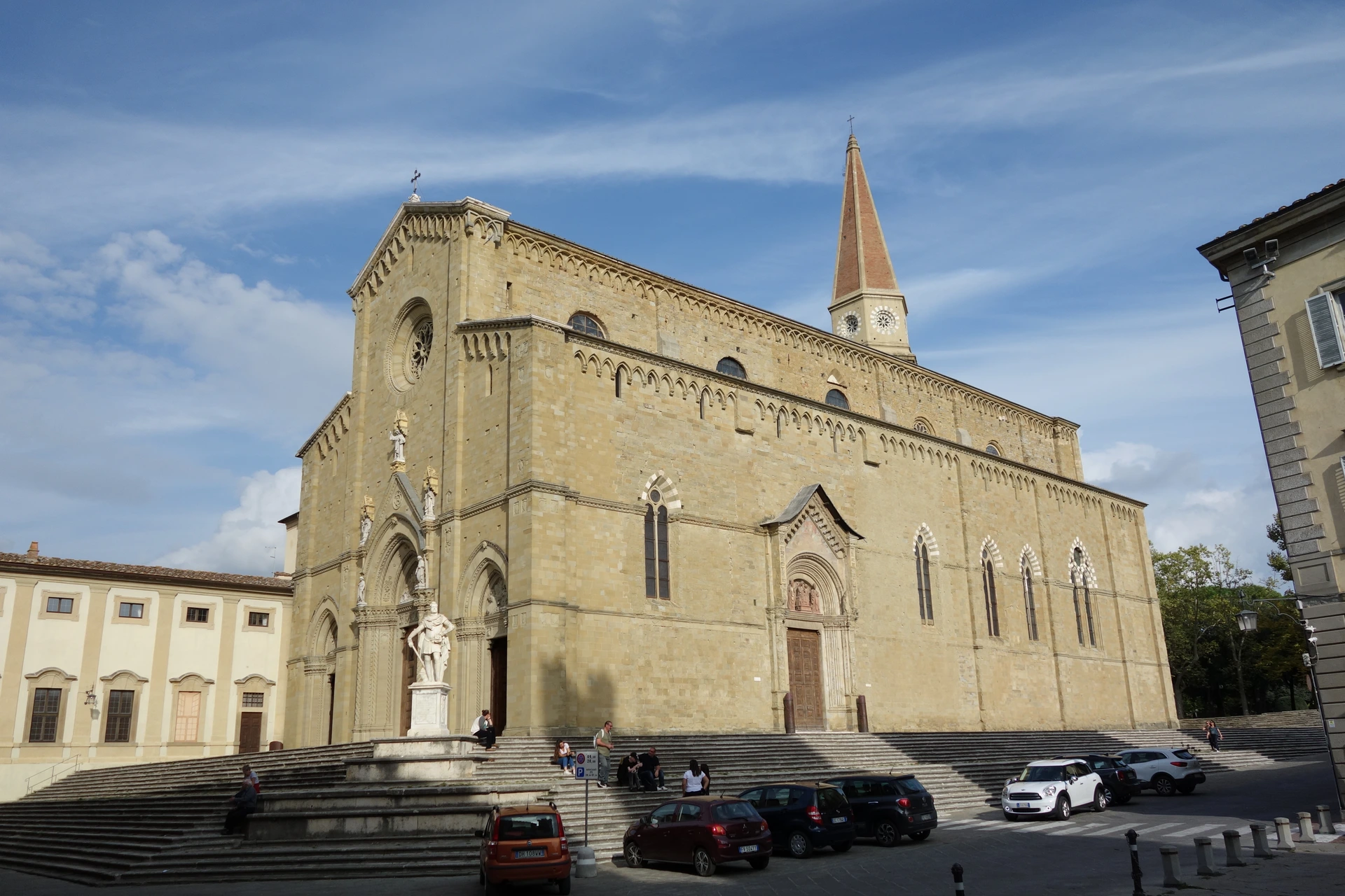 Arezzo Cathedral with its stone steps, bell tower and parked cars beside the square — Spike / Wikimedia Commons, CC BY-SA 4.0