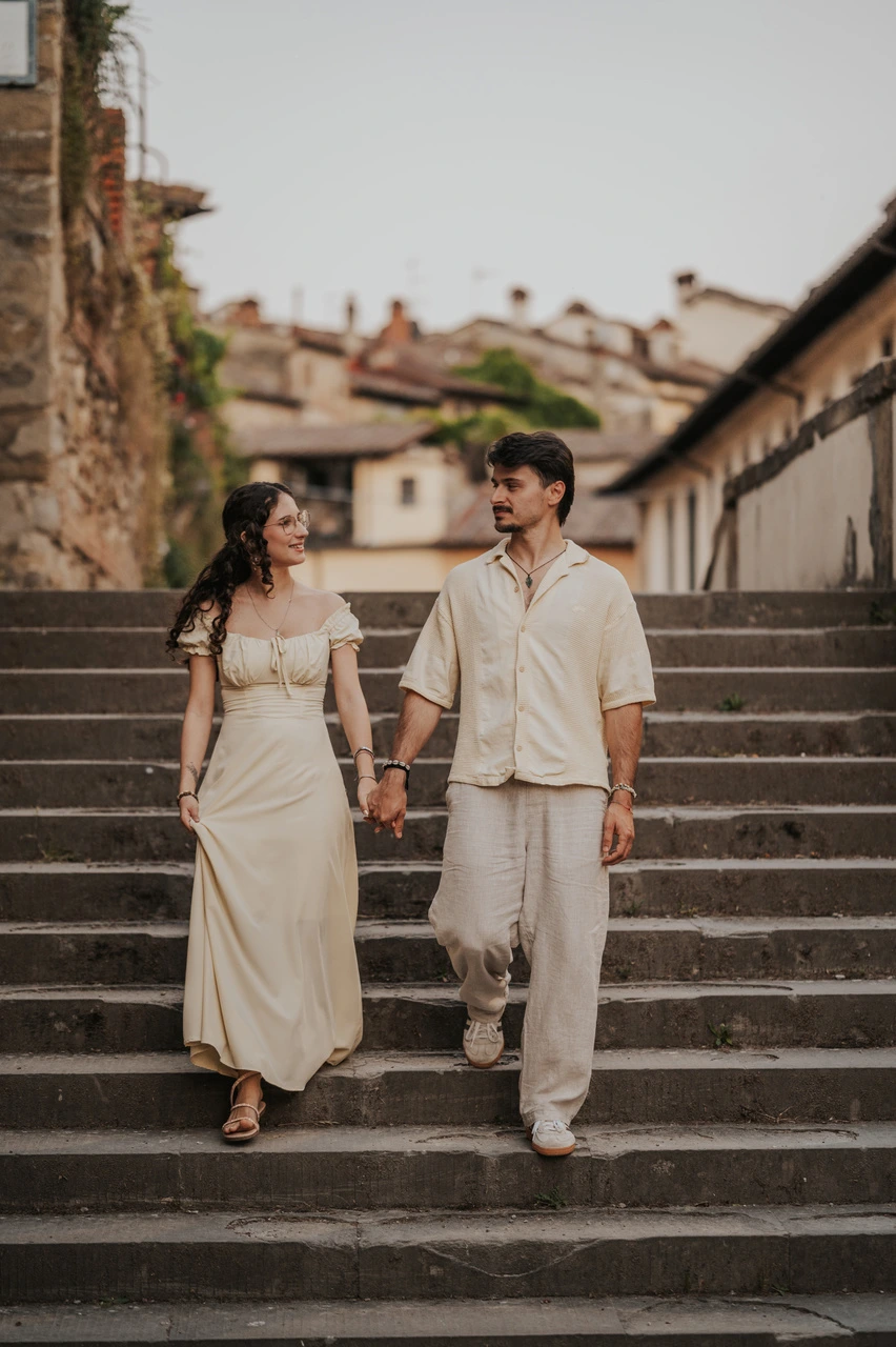Couple walking hand in hand down broad stone steps during a photoshoot in Arezzo.