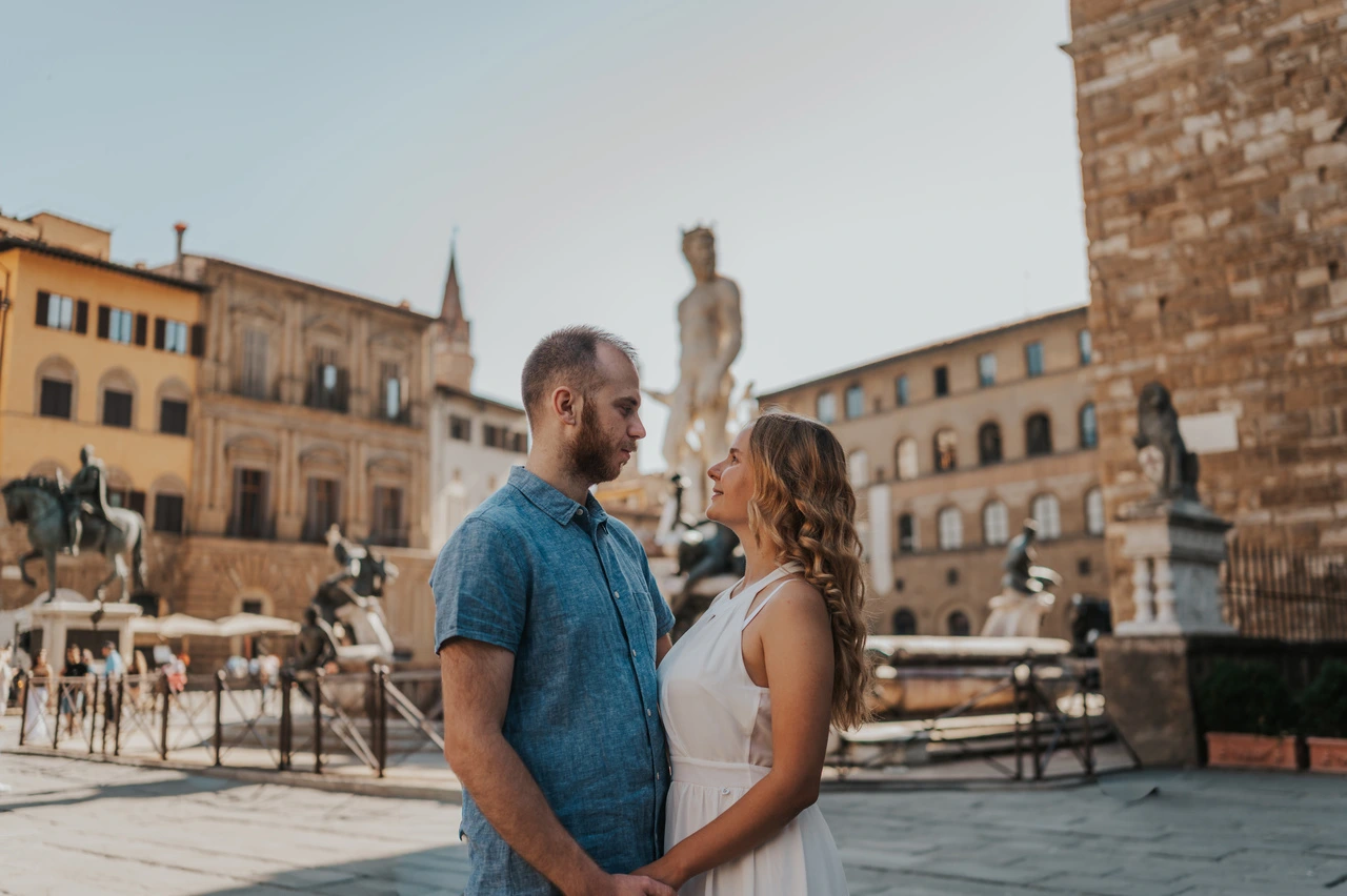 Un couple se tient la main sur la Piazza della Signoria, devant la fontaine de Neptune et le Palazzo Vecchio, lors d’une séance photo à Florence.