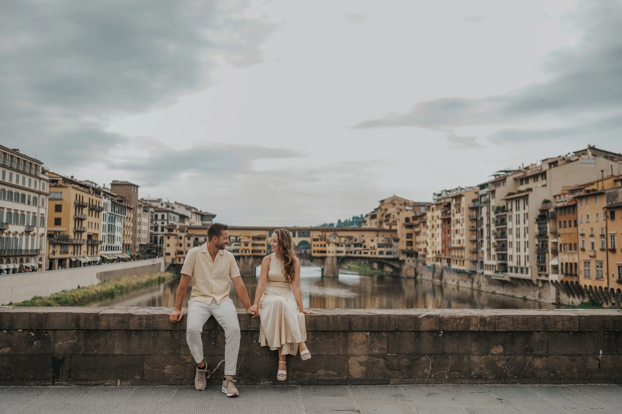 Para siedzi na kamiennym murku nad Arno, z Ponte Vecchio w tle, podczas sesji zdjęciowej we Florencji.