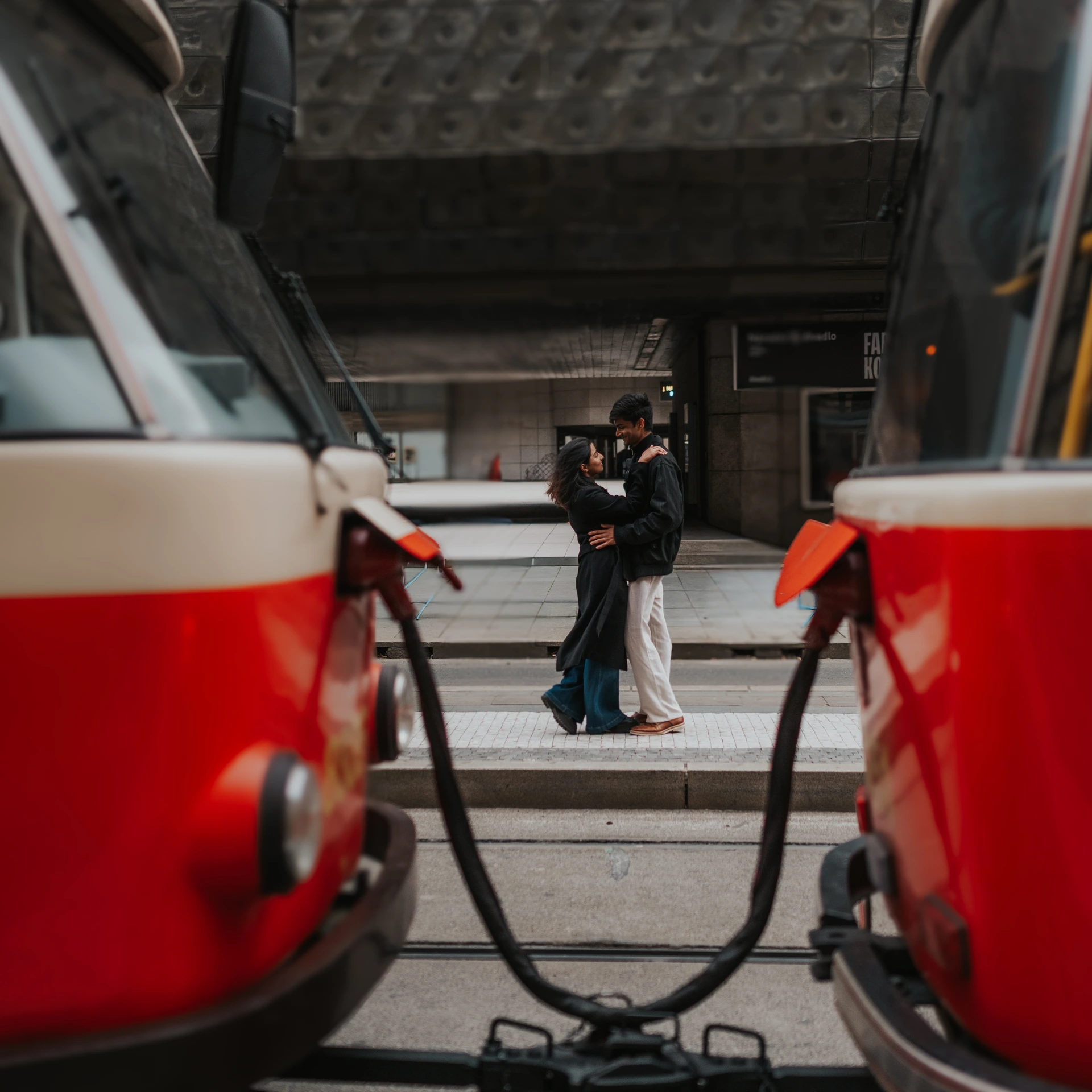 Couple embracing in Prague, framed on both sides by two red-and-white trams.