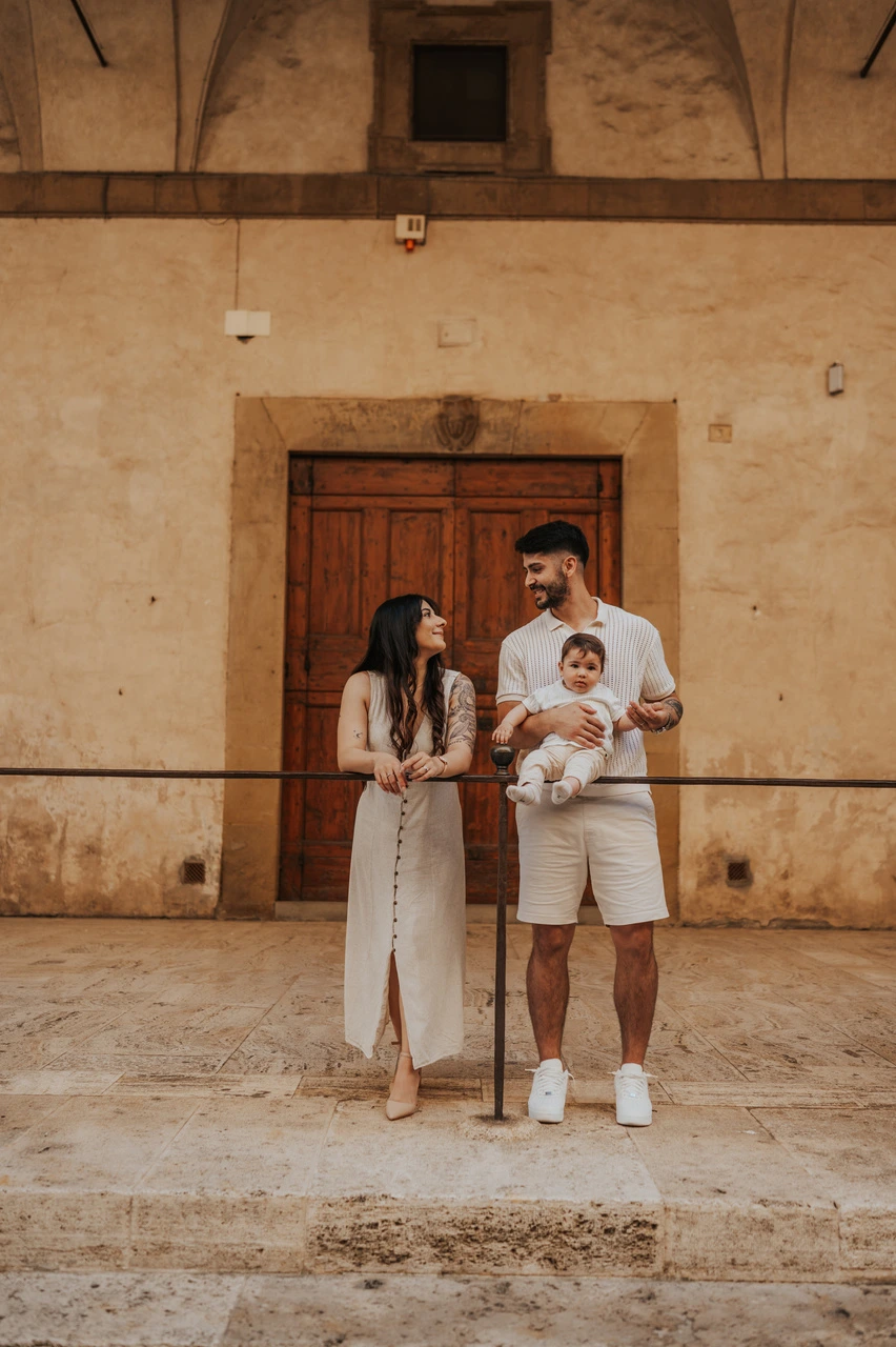 Parents holding their baby beside an old wooden doorway during a family photoshoot in Arezzo.