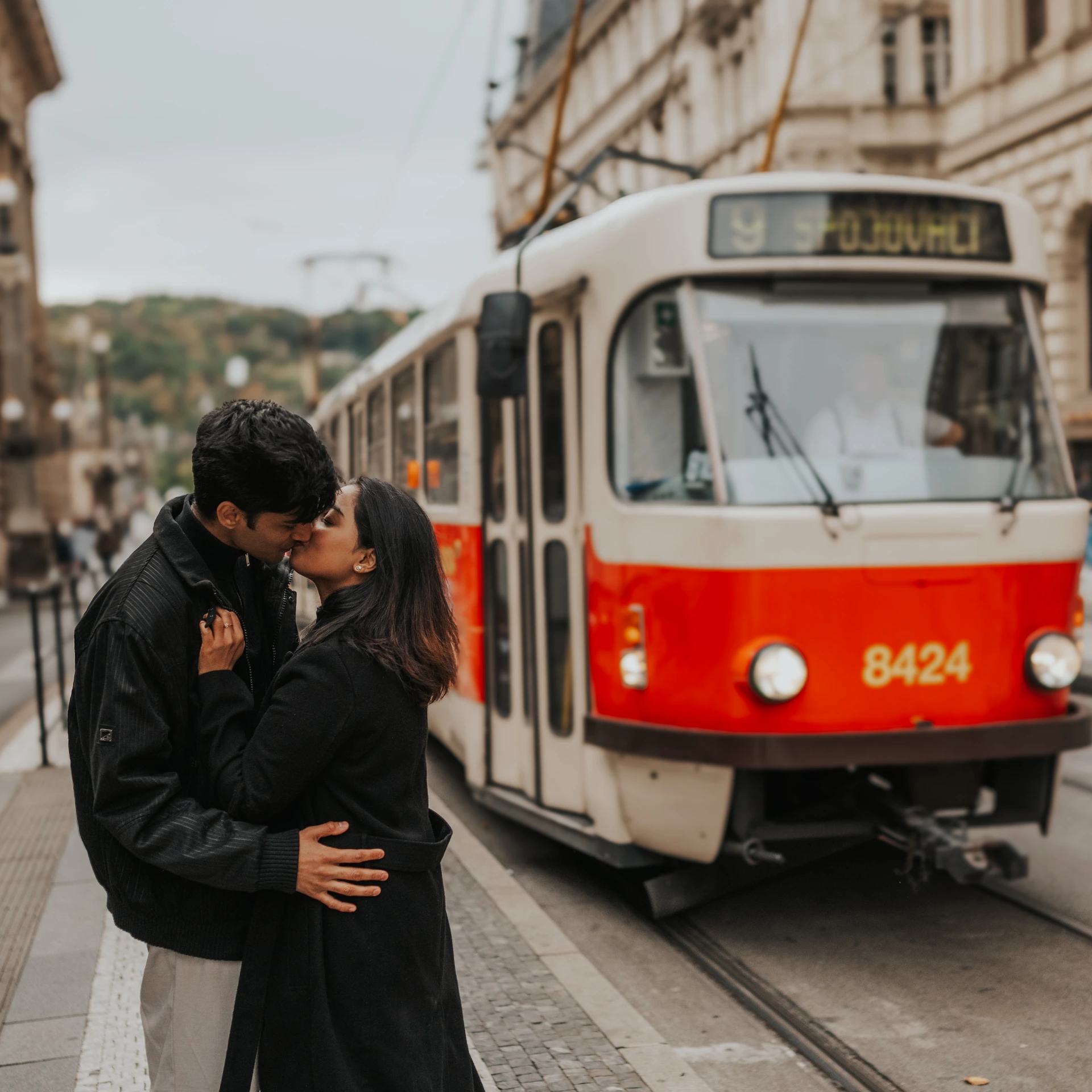 Couple kissing in front of a red-and-white tram on a street in Prague.