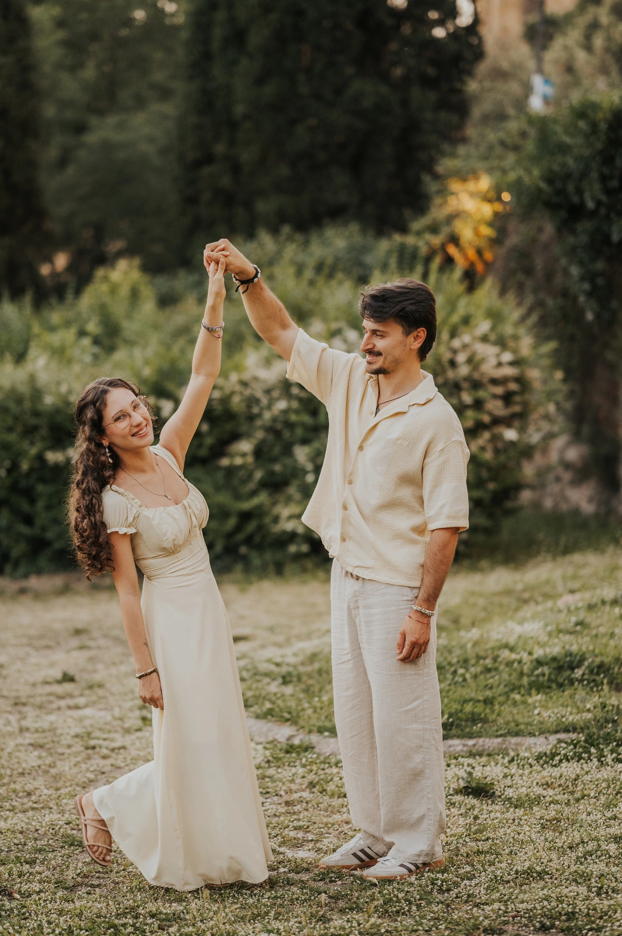 Couple dancing on the grass beneath trees during a relaxed photoshoot in Arezzo.