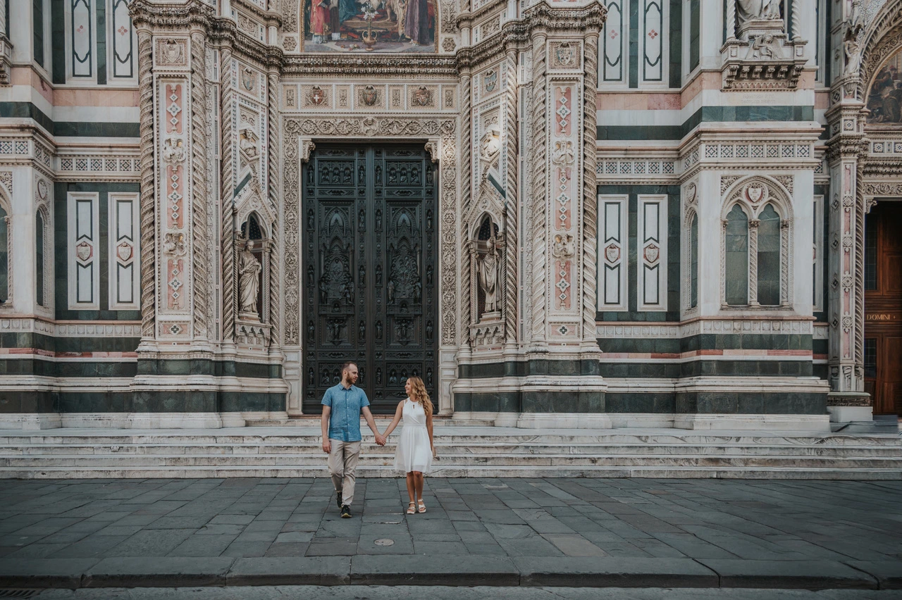 Para trzyma się za ręce na schodach przed ozdobną fasadą Duomo podczas sesji zdjęciowej we Florencji.