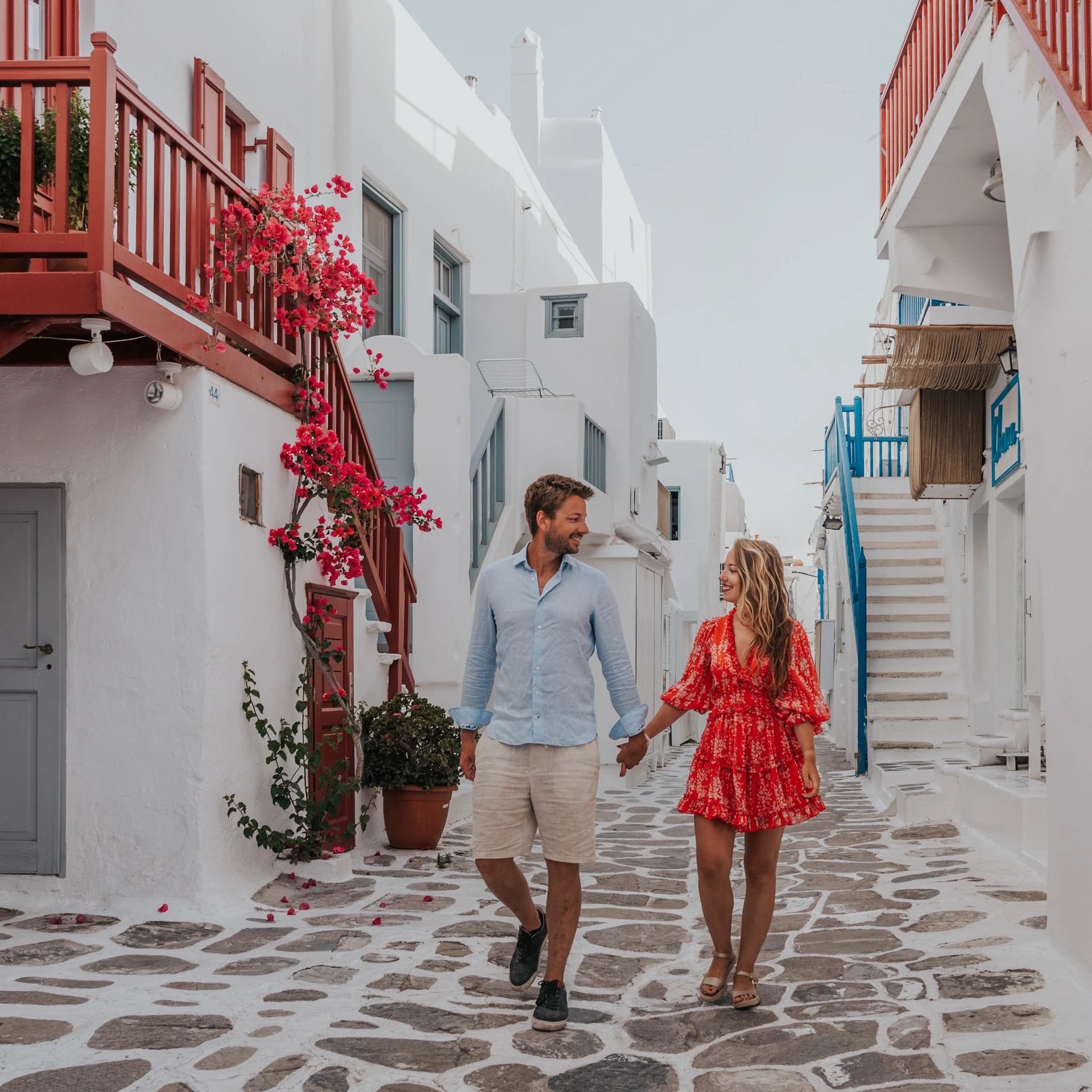 Couple walking past red balconies in the streets of Mykonos Town