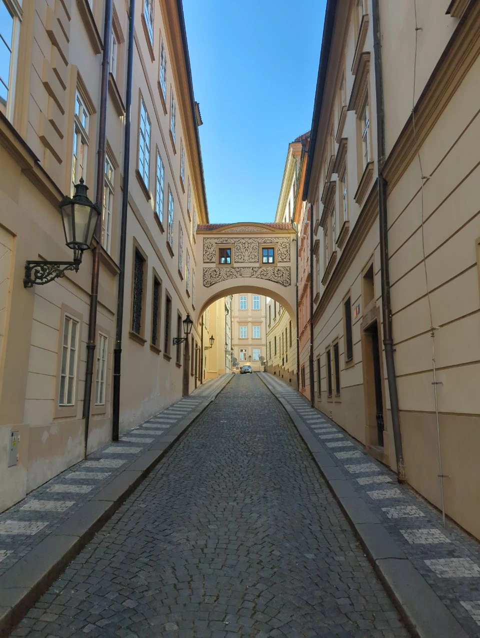 Spokojna brukowana ulica ze zdobionym łukiem przy Zamku Praskim
