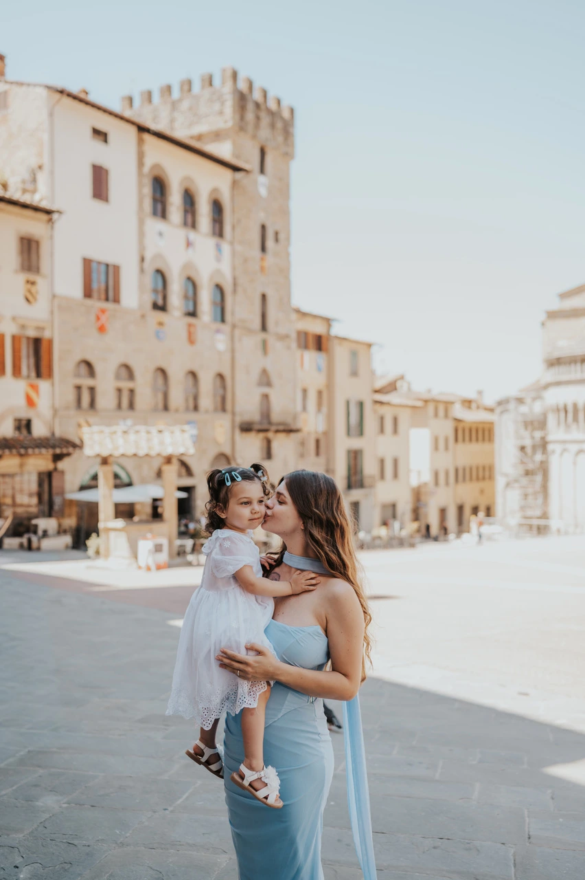 Mère en robe bleue tenant son bébé sur Piazza Grande lors d’une séance photo en famille à Arezzo.