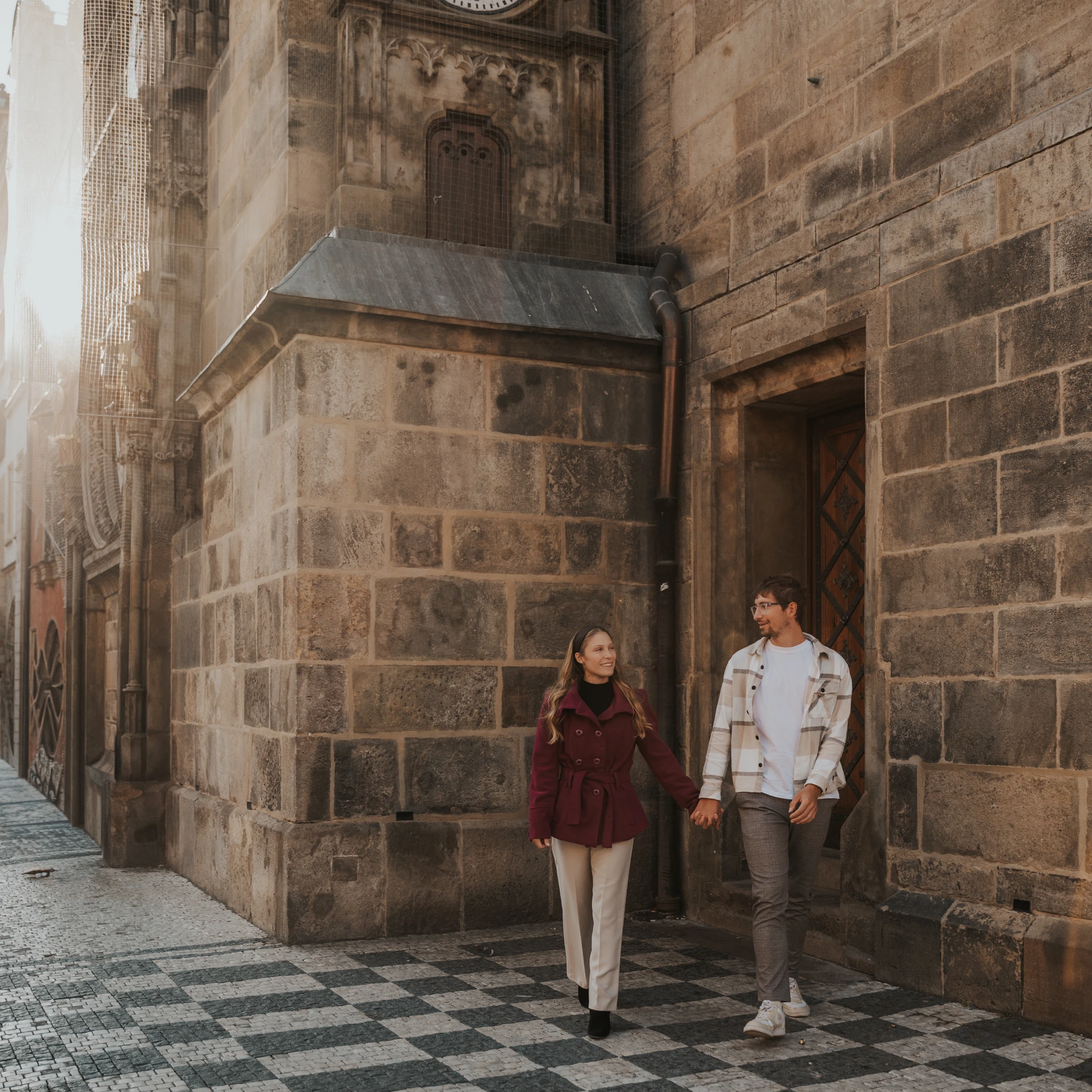 Couple walking hand in hand beside the stone facade of Prague Old Town Hall, next to the Astronomical Clock.