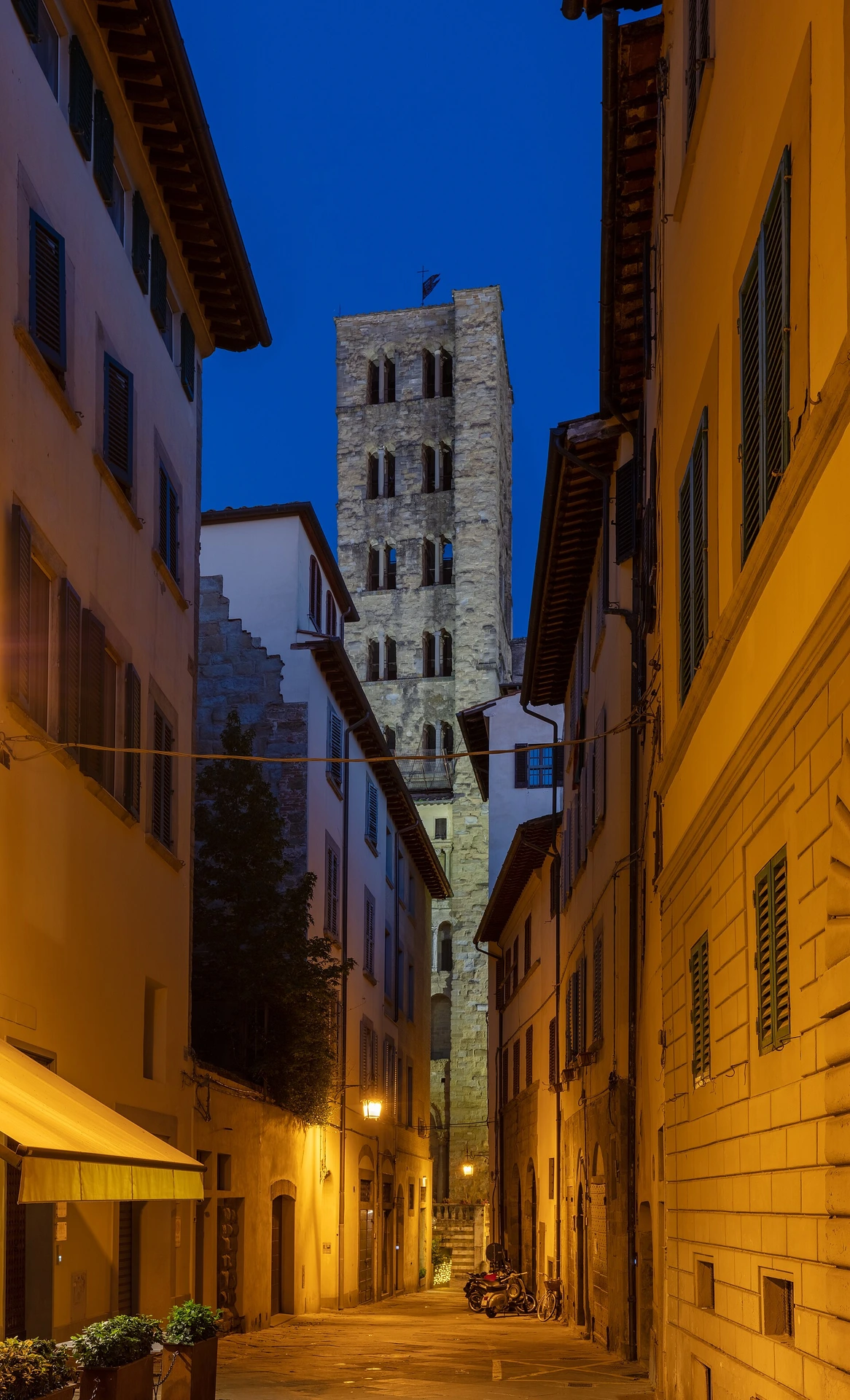 The tower of Santa Maria della Pieve above an illuminated street in Arezzo at dusk — Diego Delso / Wikimedia Commons, CC BY-SA 4.0