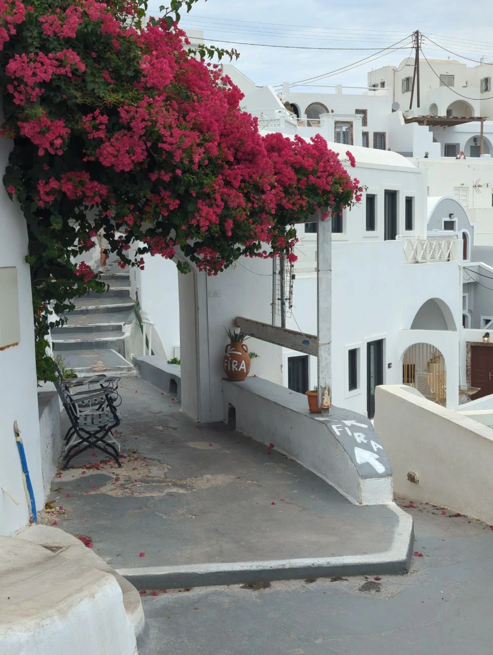 Fleurs roses au-dessus d’un passage blanc avec escalier à Imerovigli
