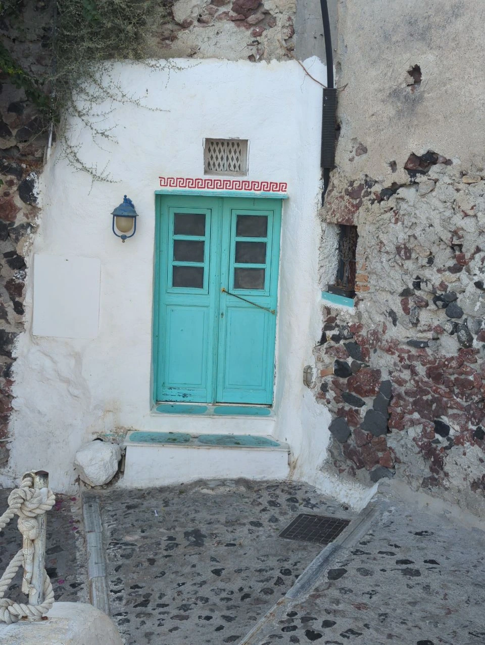 Türkisfarbene Tür in einer weißen Steinwand in Oia
