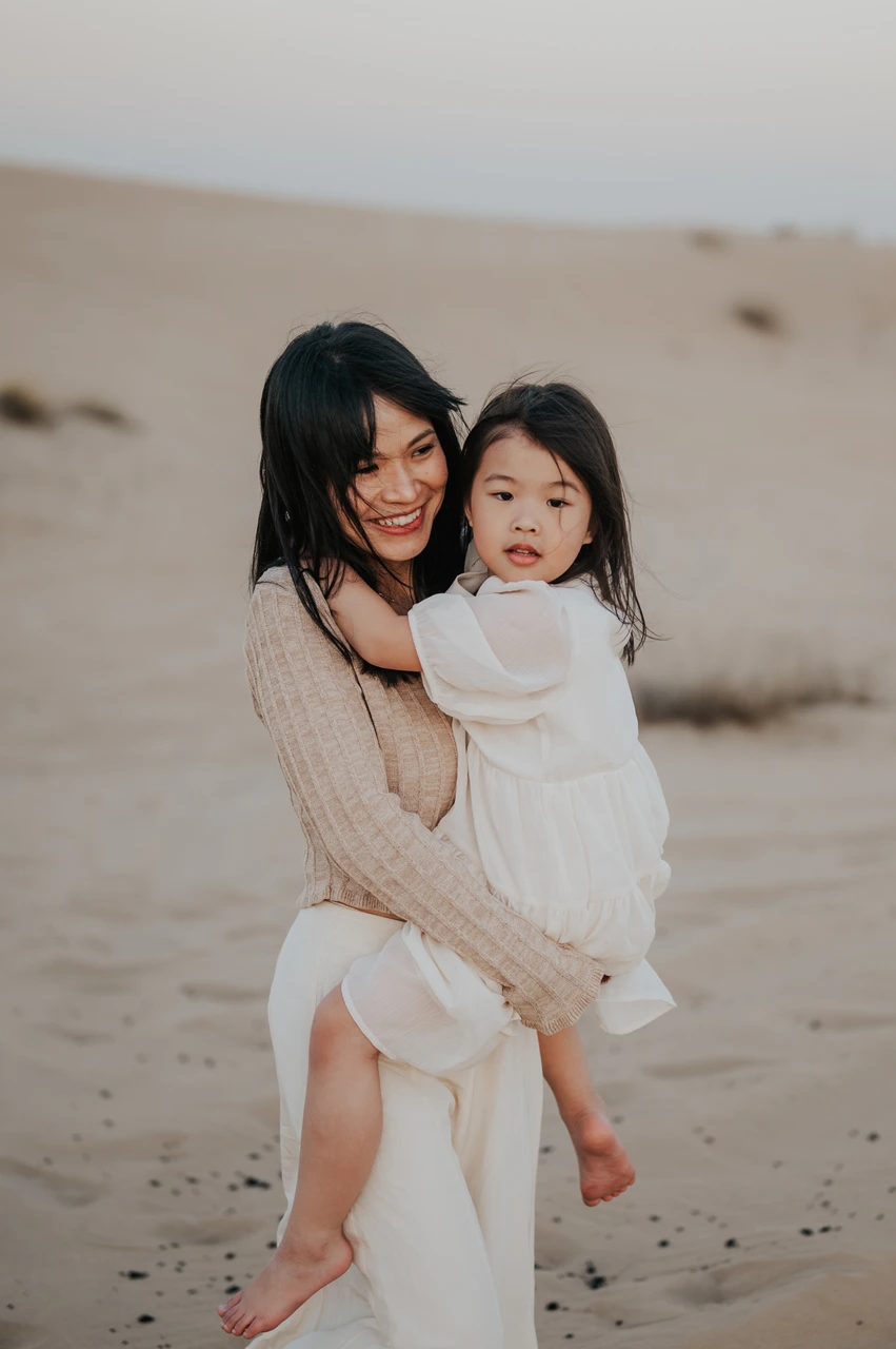 Mothers day gift ideas Dubai - Candid mother and child portrait A smiling mother holds her young daughter in the Dubai desert during a warm golden-hour family photoshoot.