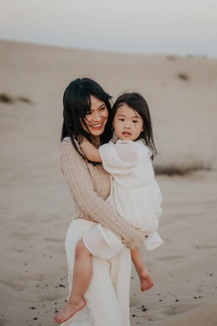 A smiling mother holds her young daughter in the Dubai desert during a warm golden-hour family photoshoot.