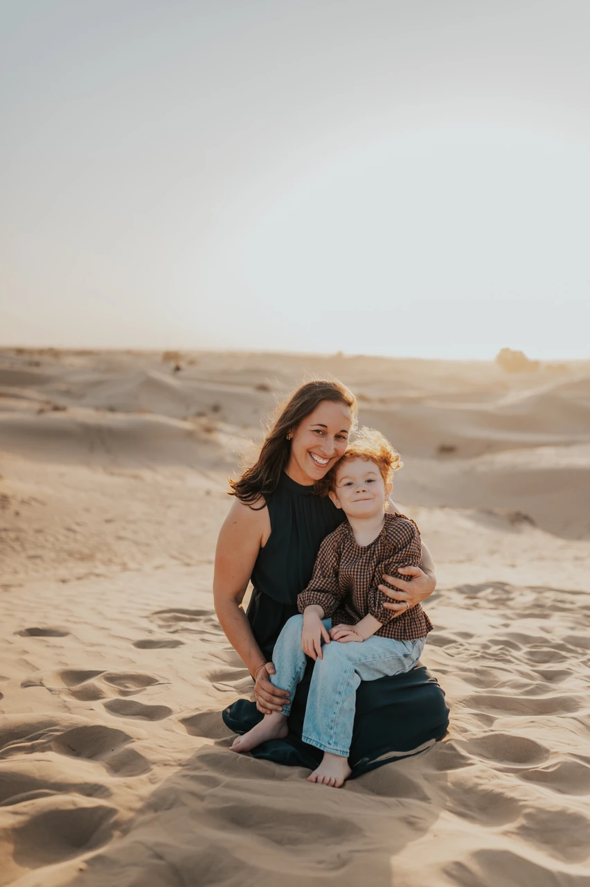 Mothers day gift ideas Dubai - Mother and son desert portrait A mother in a dark dress sits on Dubai sand dunes with her little son during a sunset family photoshoot.