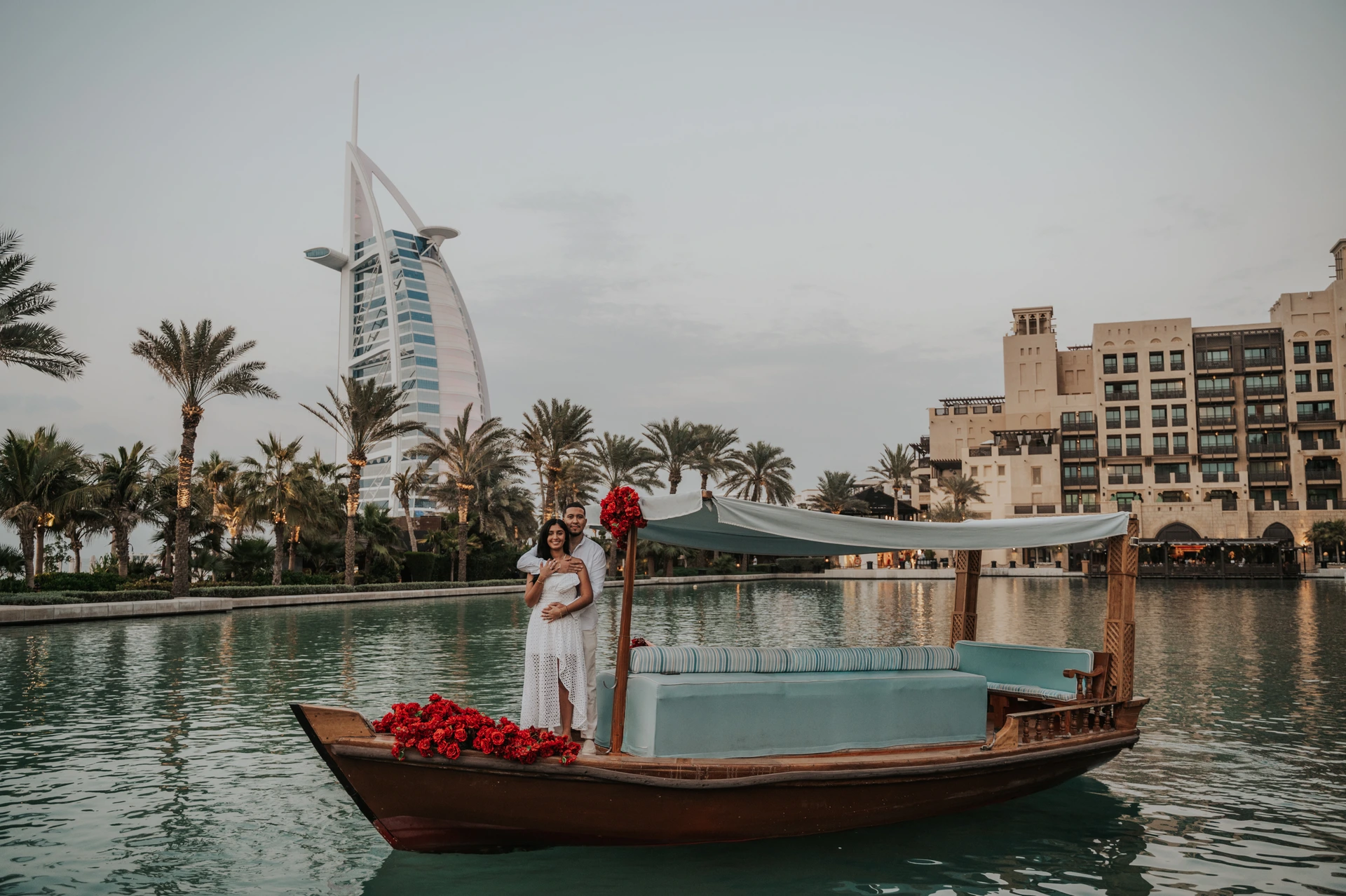 Abra Proposal at Souk Madinat Dubai - Wide Lagoon View A wide view of a decorated abra with a couple in Souk Madinat lagoon and Burj Al Arab in the distance.