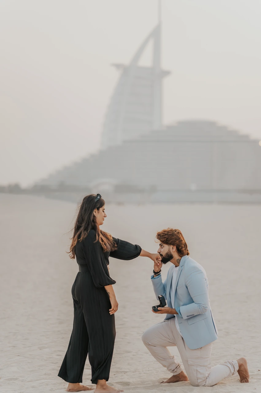 Affordable proposal Dubai - Kneeling beach proposal near Burj Al Arab A man kneels on the beach to propose while his partner smiles, with Burj Al Arab visible in the background.