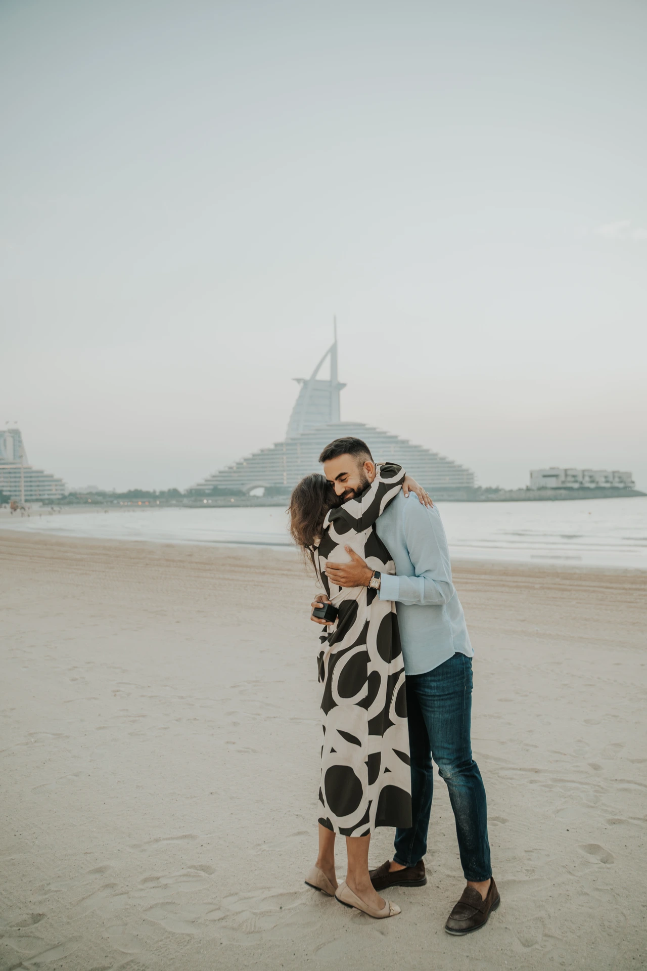 Affordable proposal Dubai - Post-proposal embrace on the beach A couple hugs on a Dubai beach after the proposal, smiling in front of Burj Al Arab at dusk.