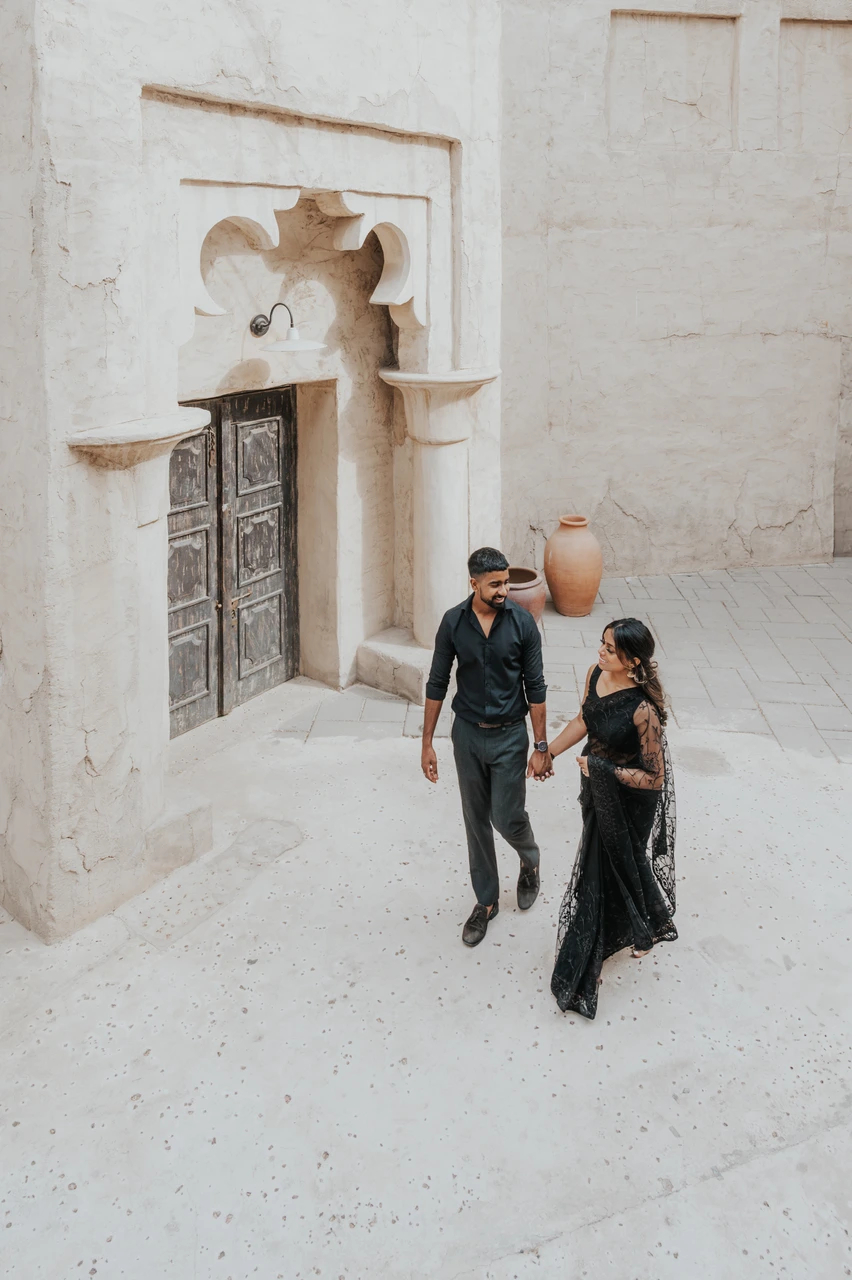 Indoor vs outdoor couple photoshoot dubai - Old Dubai walking shot A couple walks through a quiet Old Dubai lane with traditional architecture in Al Seef.