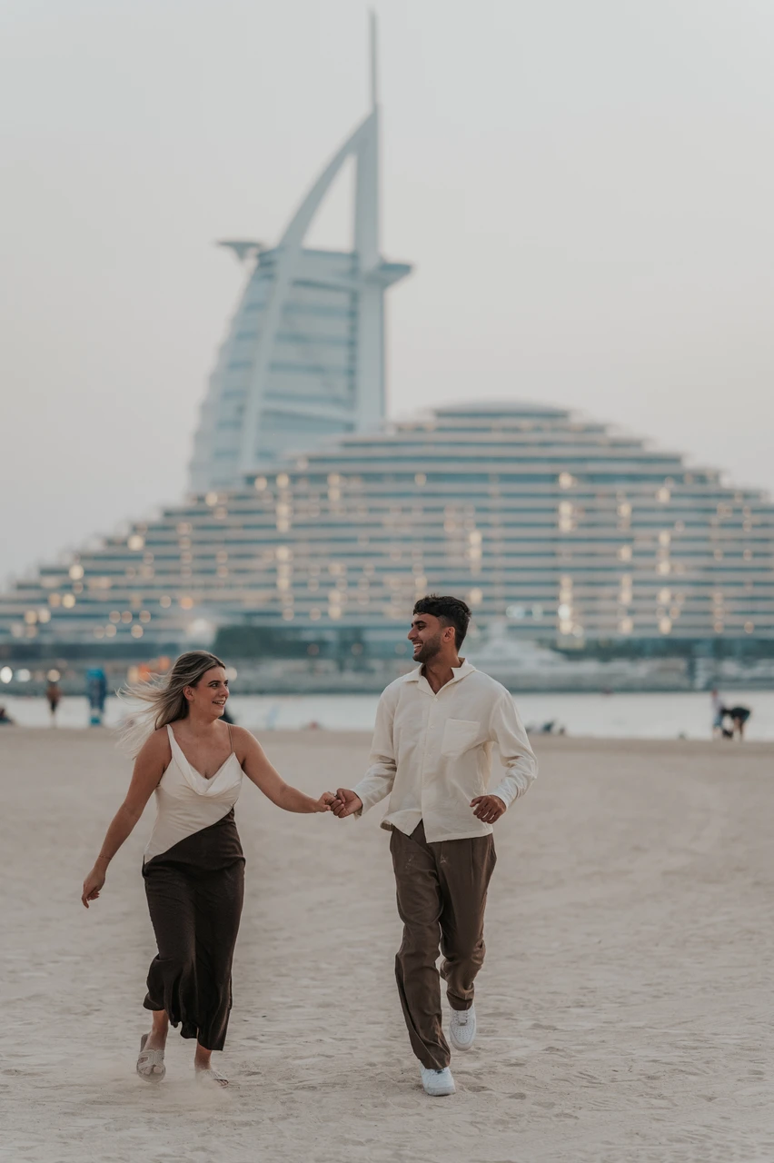 Proposal at Shimmers - pre-proposal shoreline walk A couple walks along the shoreline before a proposal at Shimmers in Dubai, with Burj Al Arab and sunset tones behind them.