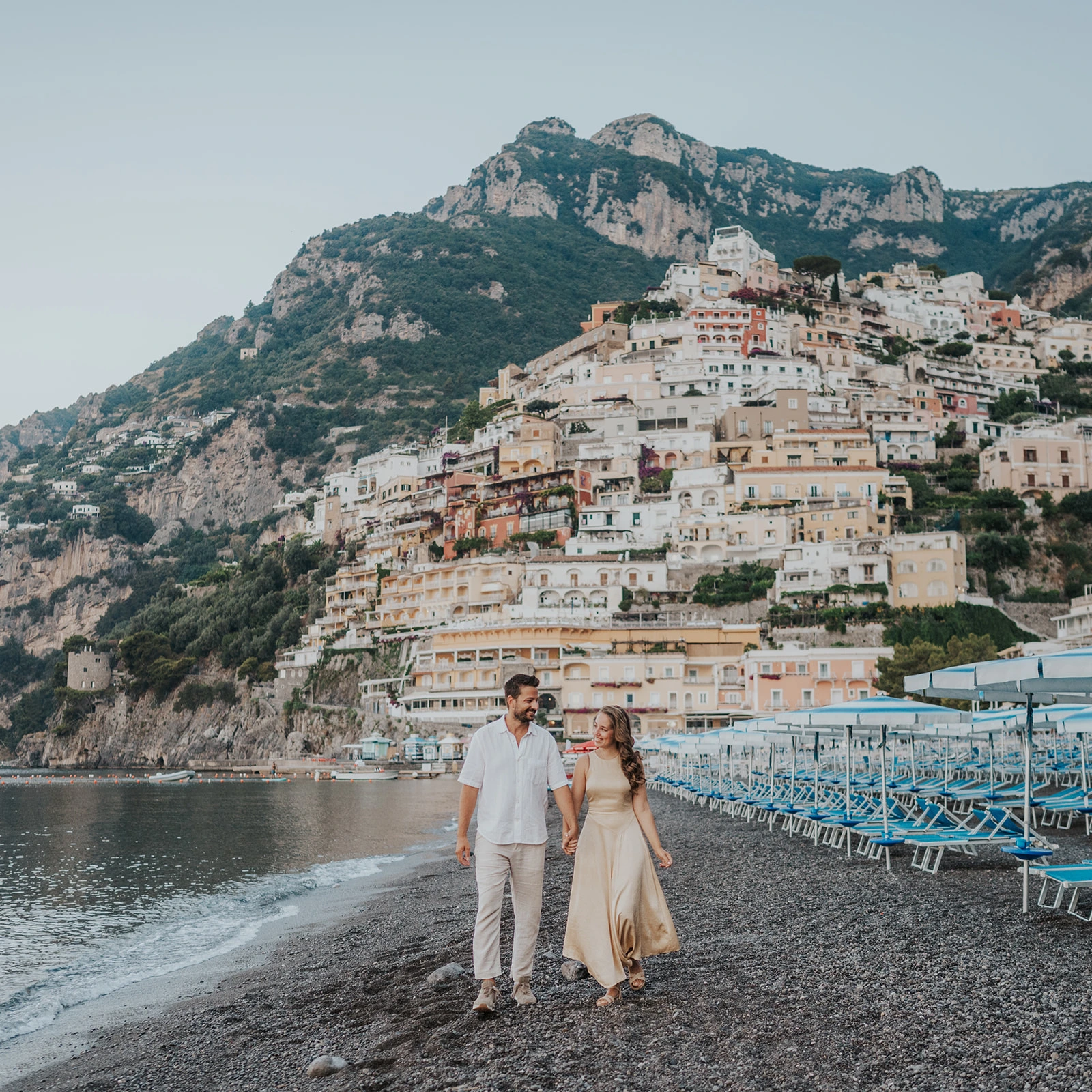Engaged couple walking on Spiaggia Grande with Positano rising behind them