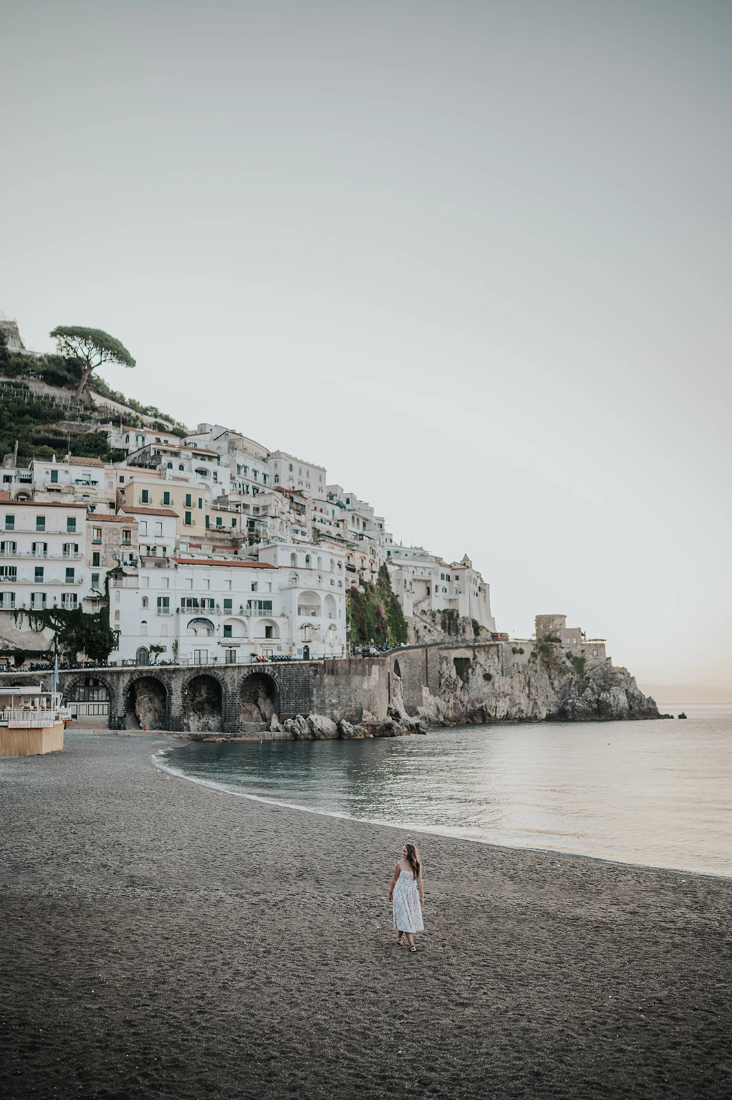 Person walking on Amalfi beach beneath the waterfront buildings