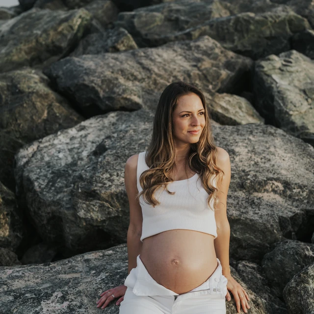 Babybauchshooting Dubai Pregnant woman sitting on rocks during outdoor maternity photoshoot in Dubai