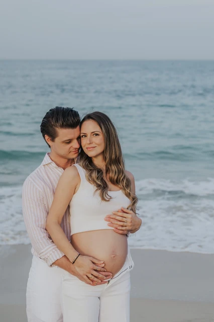 Close portrait of an expecting couple smiling together beside the sea during a Dubai babymoon beach photoshoot.