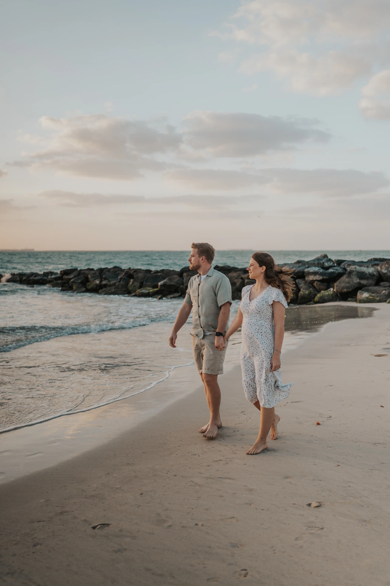 Couple walks barefoot along a quiet beach at sunset in Dubai, capturing a relaxed maternity session by the sea.