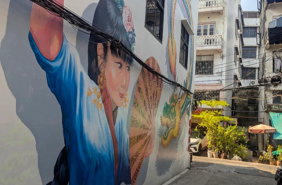 A mural of a woman with a fan and dragon fills one side of a narrow Talat Noi lane in Bangkok.