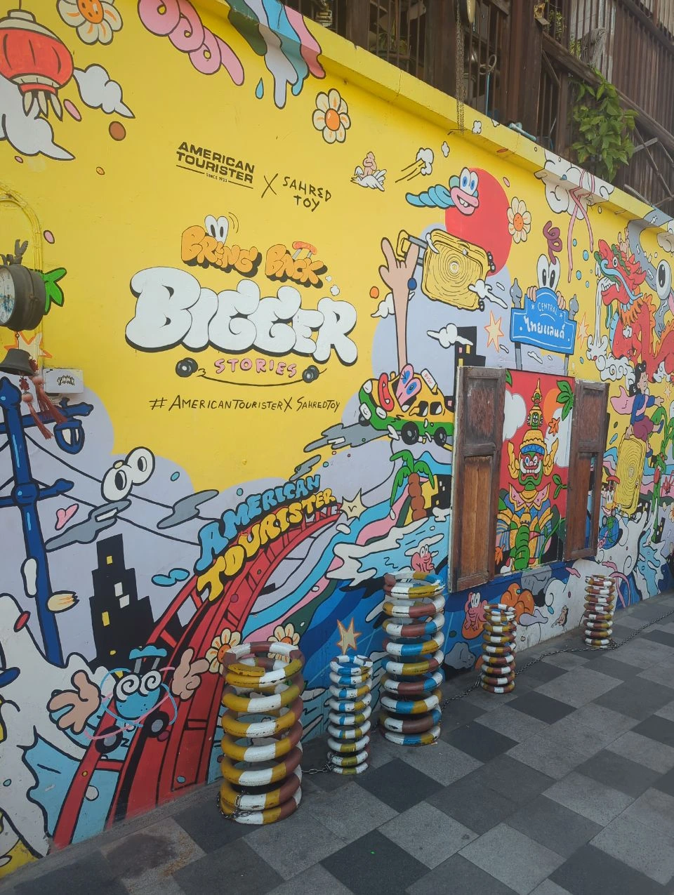 Talat Noi Photoshoot Guide - Yellow Street Art Bright yellow street art with cartoon figures, painted lettering and colourful stacked rings lines a narrow Talat Noi passage in Bangkok.