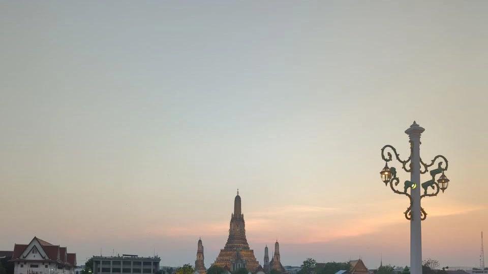 Wat Arun glows beneath a warm evening sky beside an illuminated riverfront lamp, setting the scene for a Bangkok proposal.