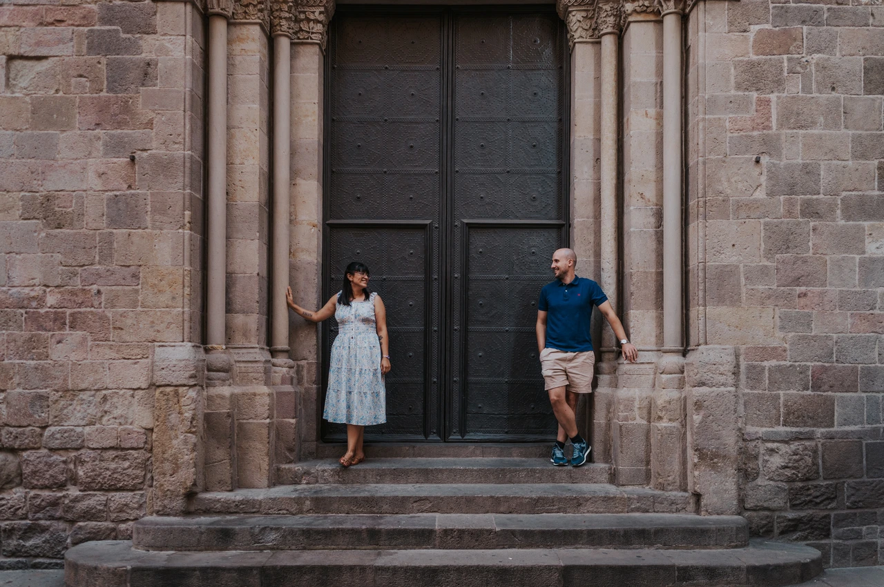 Together beside an ornate Gothic Quarter doorway | Barcelona anniversary photoshoot The couple standing on the steps on either side of a dark wooden door framed by stone columns in the Gothic Quarter during their anniversary photoshoot in Barcelona.