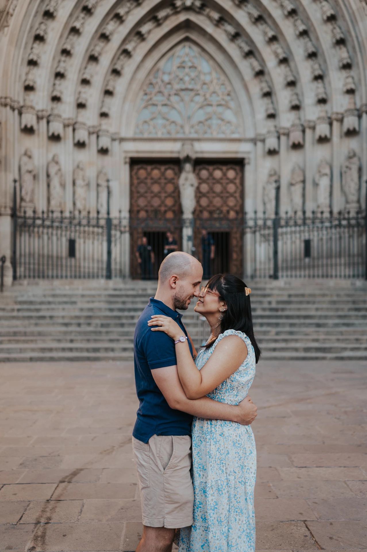 The couple kissing in front of the steps and carved Gothic entrance of Barcelona Cathedral during their anniversary photoshoot in Barcelona.