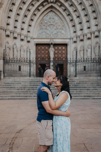 The couple kissing in front of the steps and carved Gothic entrance of Barcelona Cathedral during their anniversary photoshoot in Barcelona.