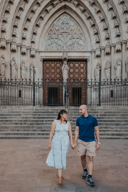 A walk together in front of Barcelona Cathedral | Barcelona anniversary photoshoot The couple smiling at each other as they walk hand in hand in front of Barcelona Cathedral during their anniversary photoshoot in Barcelona.