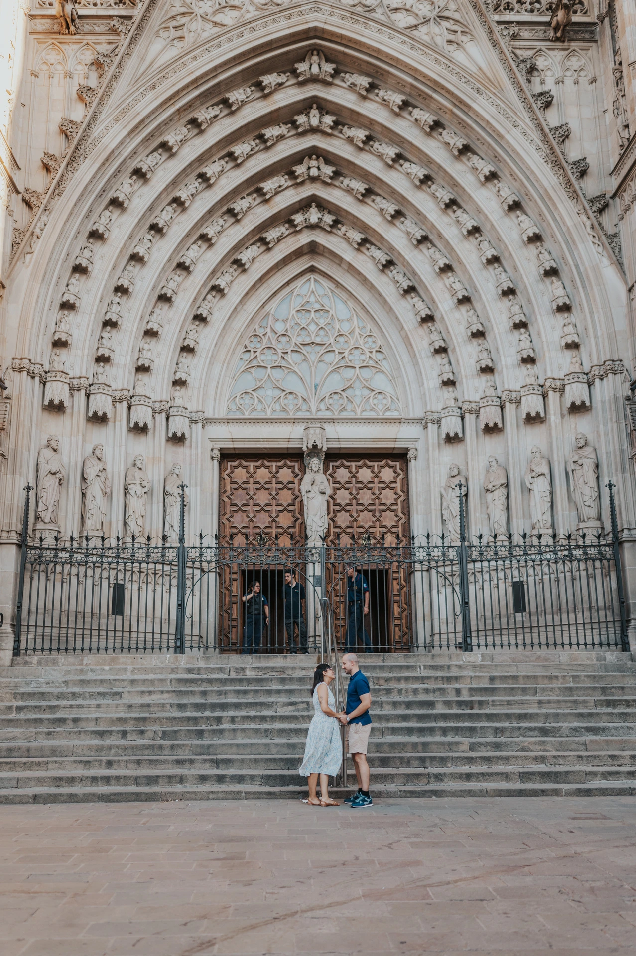 The couple embracing at the foot of the broad steps beneath Barcelona Cathedral’s ornate entrance during their anniversary photoshoot in Barcelona.