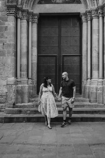 Hand in hand on the old town’s doorway steps in black and white | Barcelona anniversary photoshoot Black-and-white photograph: the couple holding hands on the steps in front of a carved arched doorway in the Gothic Quarter during their anniversary photoshoot in Barcelona.