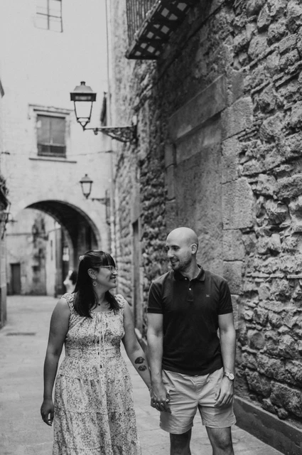 A walk through a narrow old-town lane in black and white | Barcelona anniversary photoshoot A black-and-white portrait of the couple holding hands beside a textured stone wall in a narrow Gothic Quarter lane during their anniversary photoshoot in Barcelona.