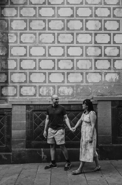 Hand in hand against a patterned old-town wall in black and white | Barcelona anniversary photoshoot Black-and-white photograph: the couple walking hand in hand beside a patterned stone wall in the Gothic Quarter during their anniversary photoshoot in Barcelona.