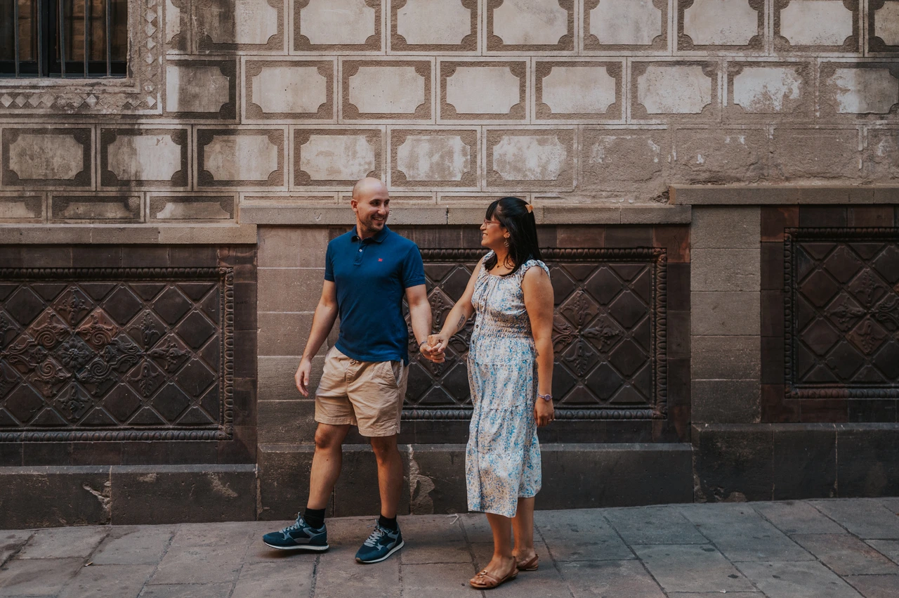 Hand in hand against a patterned old-town wall | Barcelona anniversary photoshoot The couple walking hand in hand beside a patterned stone wall in the Gothic Quarter during their anniversary photoshoot in Barcelona.