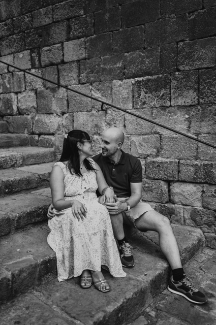 Together on the Gothic Quarter’s stone steps in black and white | Barcelona anniversary photoshoot Black-and-white photograph: the couple sitting close together on broad stone steps beside a historic wall in the Gothic Quarter during their anniversary photoshoot in Barcelona.