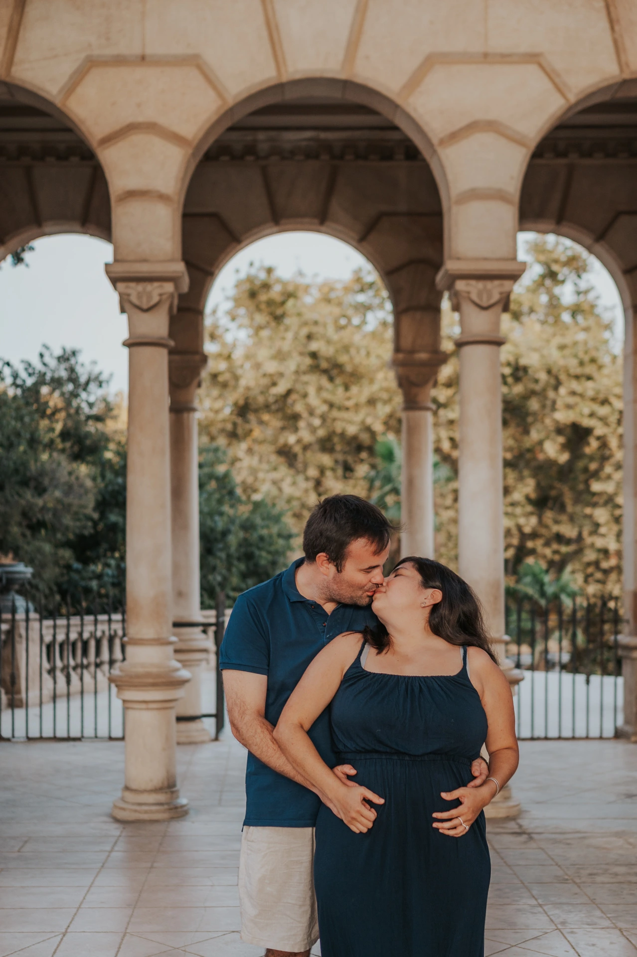 The parents standing close together beneath the stone arches during their family photoshoot in Barcelona.