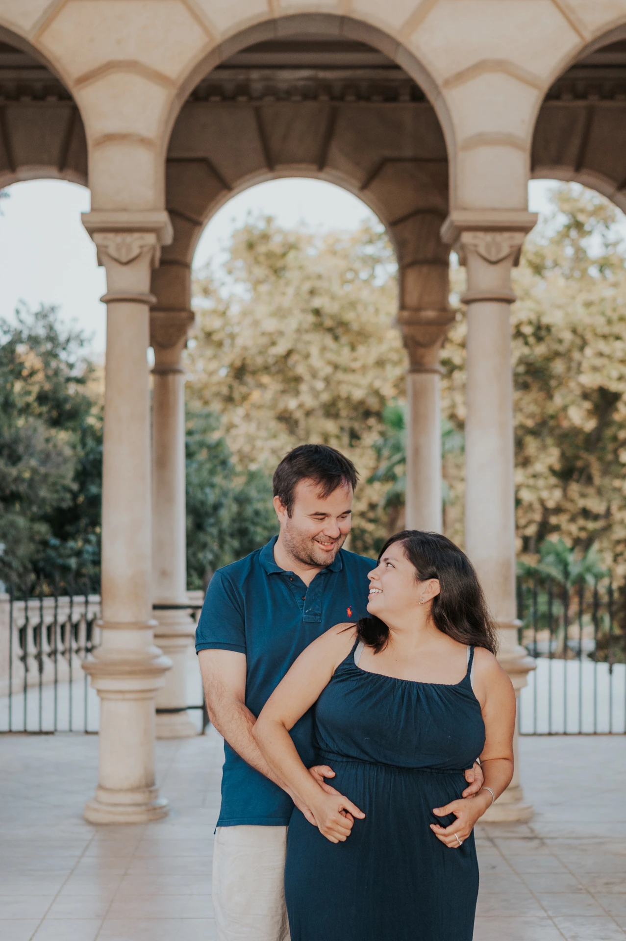 The parents standing close together beneath the stone arches during their family photoshoot in Barcelona.
