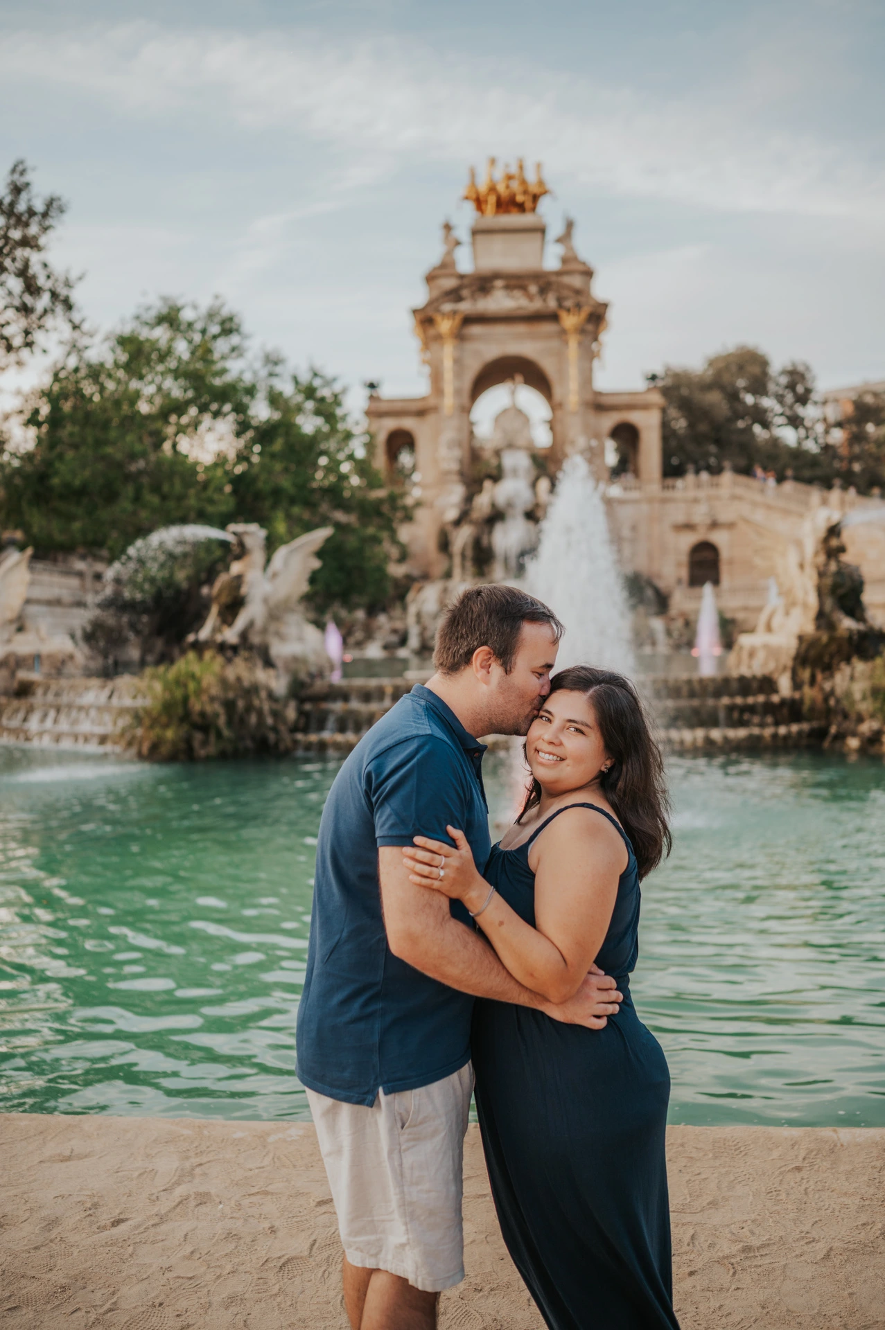 The father leaning towards the mother for a forehead kiss beside the fountain during their family photoshoot in Barcelona.