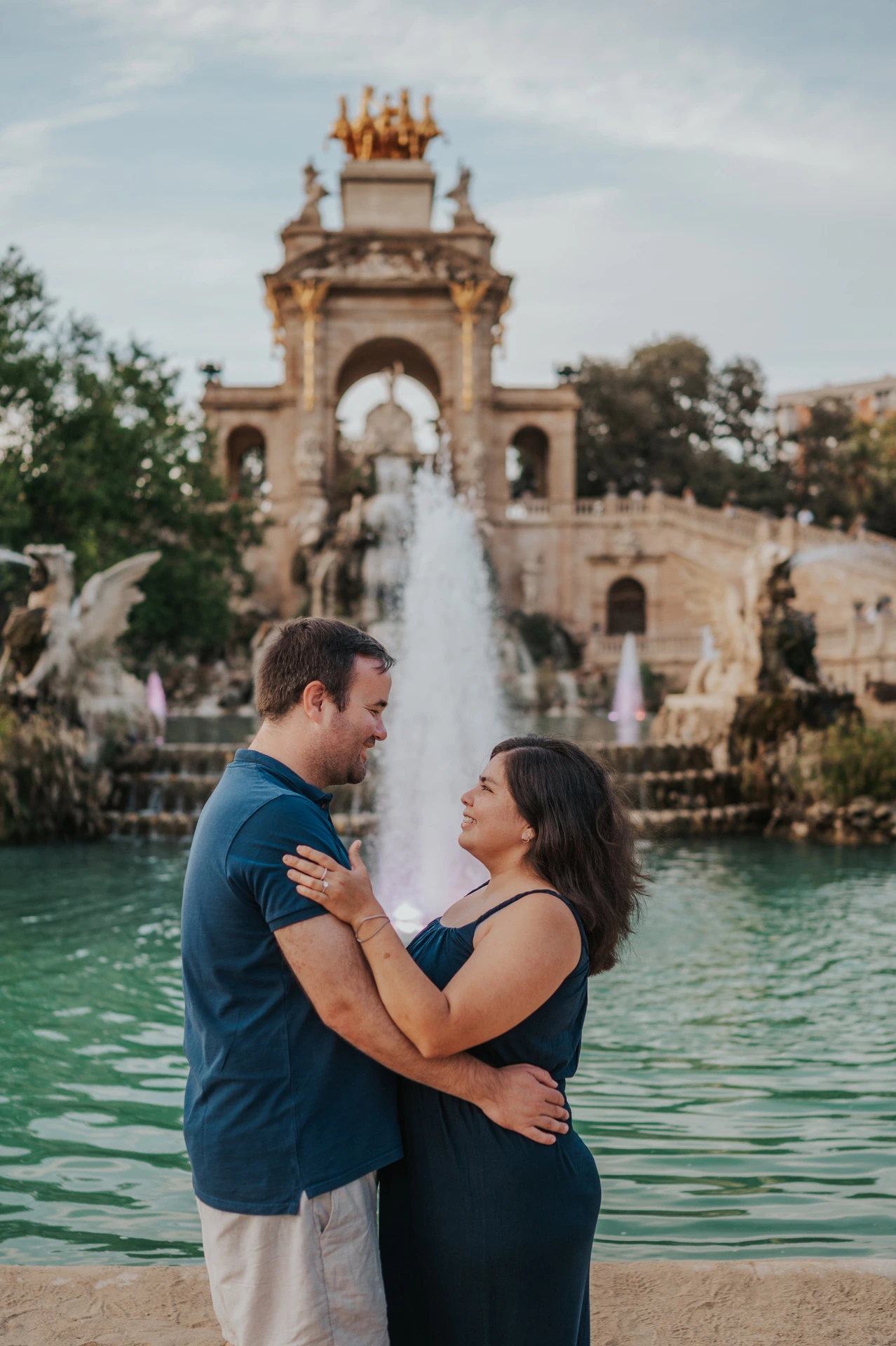 The parents smiling towards one another beside the fountain during their family photoshoot in Barcelona.